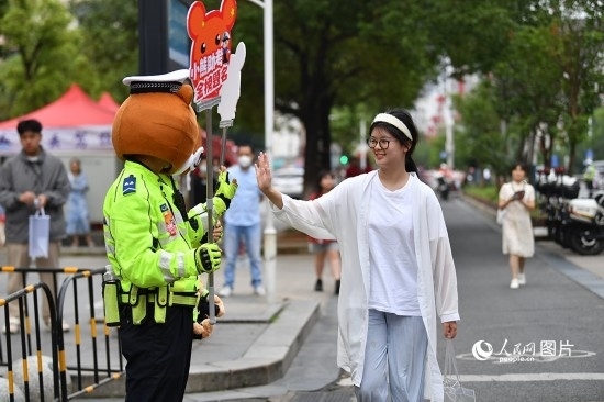 6月7日上午9時(shí)，隨著鈴聲的響起，2023年江西高考正式開考，江西省的53.57萬考生以縣（區(qū)）為單位隨機(jī)安排在全省256個(gè)考點(diǎn)、18968個(gè)考場(chǎng)參加高考。圖為“小熊交警”和考生擊掌鼓勵(lì)。 人民網(wǎng)記者 時(shí)雨攝
