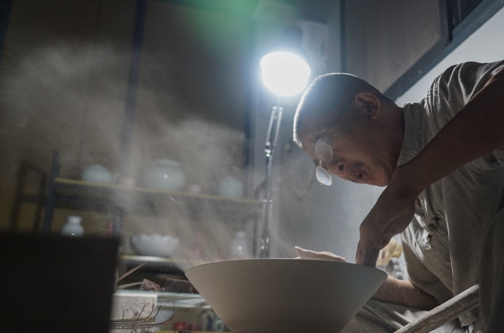 ↑ 在景德鎮(zhèn)，手工匠人吹去坯內(nèi)的泥土（2021年7月14日攝）。