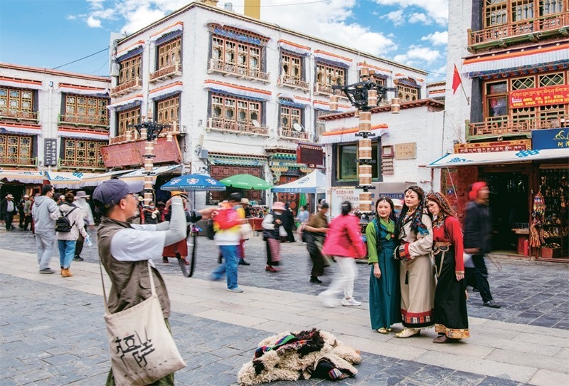 千年八廓街，見證民族團(tuán)結(jié)。2021年7月，習(xí)近平總書記來到位于西藏拉薩老城區(qū)的八廓街，感慨地說：“千年八廓街，是我們各民族建起來的八廓街。各民族文化在這里交流交往交融，我們中華民族的大家庭在這里其樂融融?！眻D為2023年6月13日，游客身著藏裝在八廓街拍照留念。 新華社記者 姜帆/攝