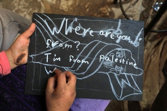 2023年12月28日，一名學(xué)生在加沙地帶南部城市拉法一所學(xué)校的臨時教室中寫下“我來自巴勒斯坦”的字樣。新華社發(fā)（里澤克·阿卜杜勒賈瓦德攝）