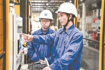 在廣西柳工機械股份有限公司生產(chǎn)車間內(nèi)，一名高級技師（右）給徒弟講解數(shù)控設(shè)備操作細節(jié)。新華社記者 曹祎銘攝